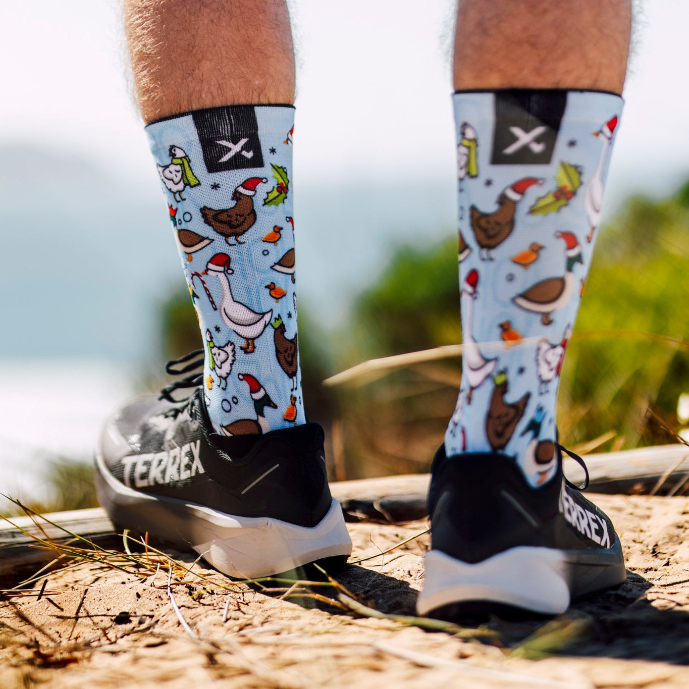 Person wearing colourful socks with Christmas patterns on a beach.